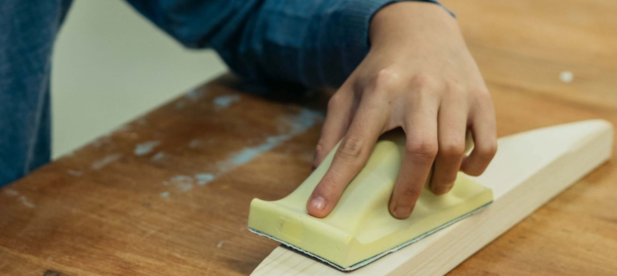 Eine Hand mit Schleif-Klotz an einem Werkstück.