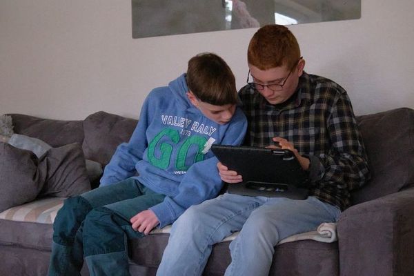 Zwei Jugendliche sitzen auf einem Sofa und schauen in ein Buch.