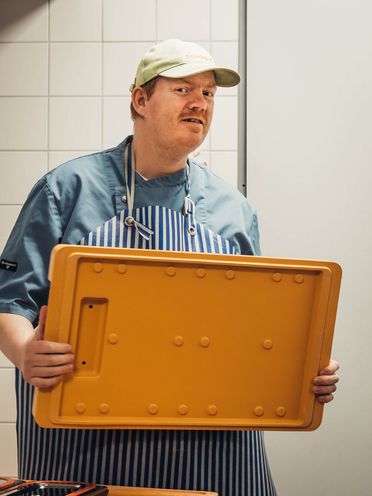 Eine Person trägt einen Wärmeboxdeckel für Essen auf Rädern.