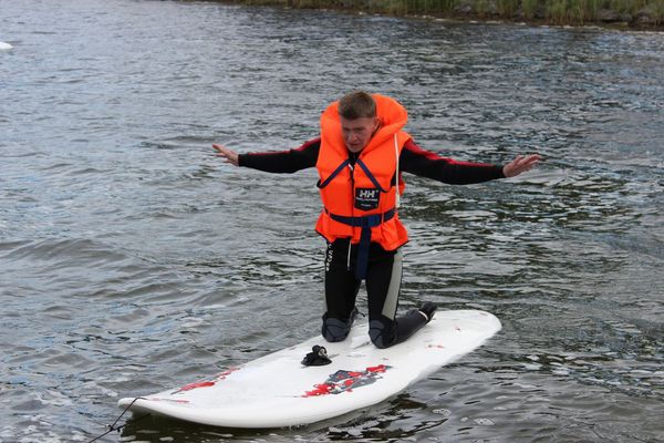 Eine Person mit ausgebreiteten Armen kniet auf einem Board im Wasser