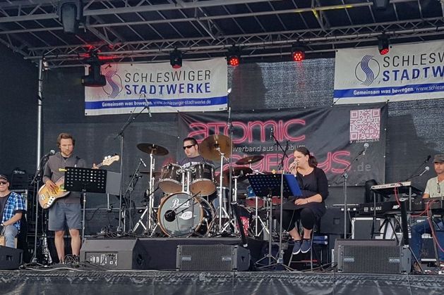 Das Foto zeigt die Band Gangway bei einem Auftritt auf einer Bühne. Im Hintergrund der Bühne hängen große Banner der Schleswiger Stadtwerke.