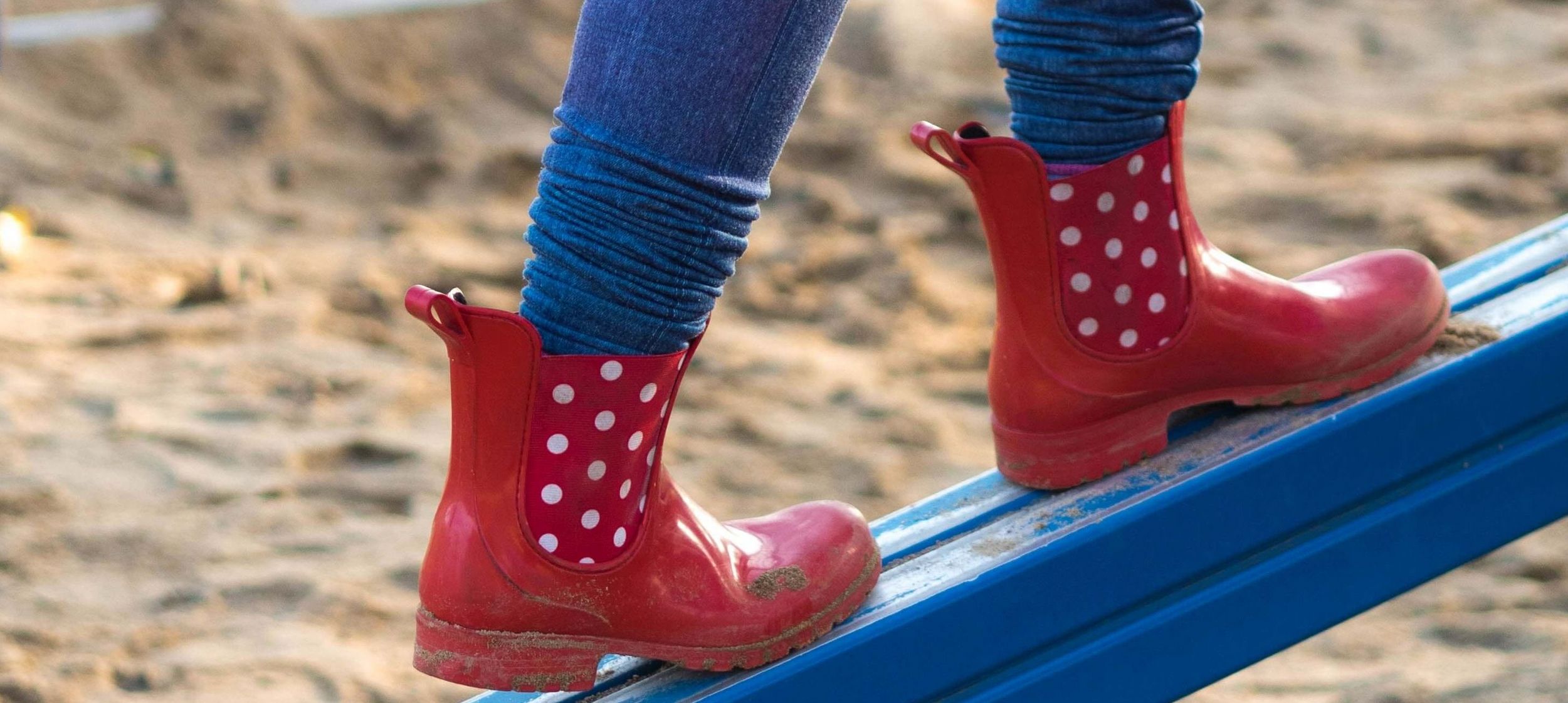 Auf schiefer Ebene balancierende rote Gummistiefel mit weißen Punkten