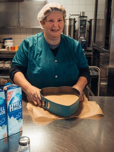 Eine Person bereitet einen Kuchen in einer Herzform vor und lacht.