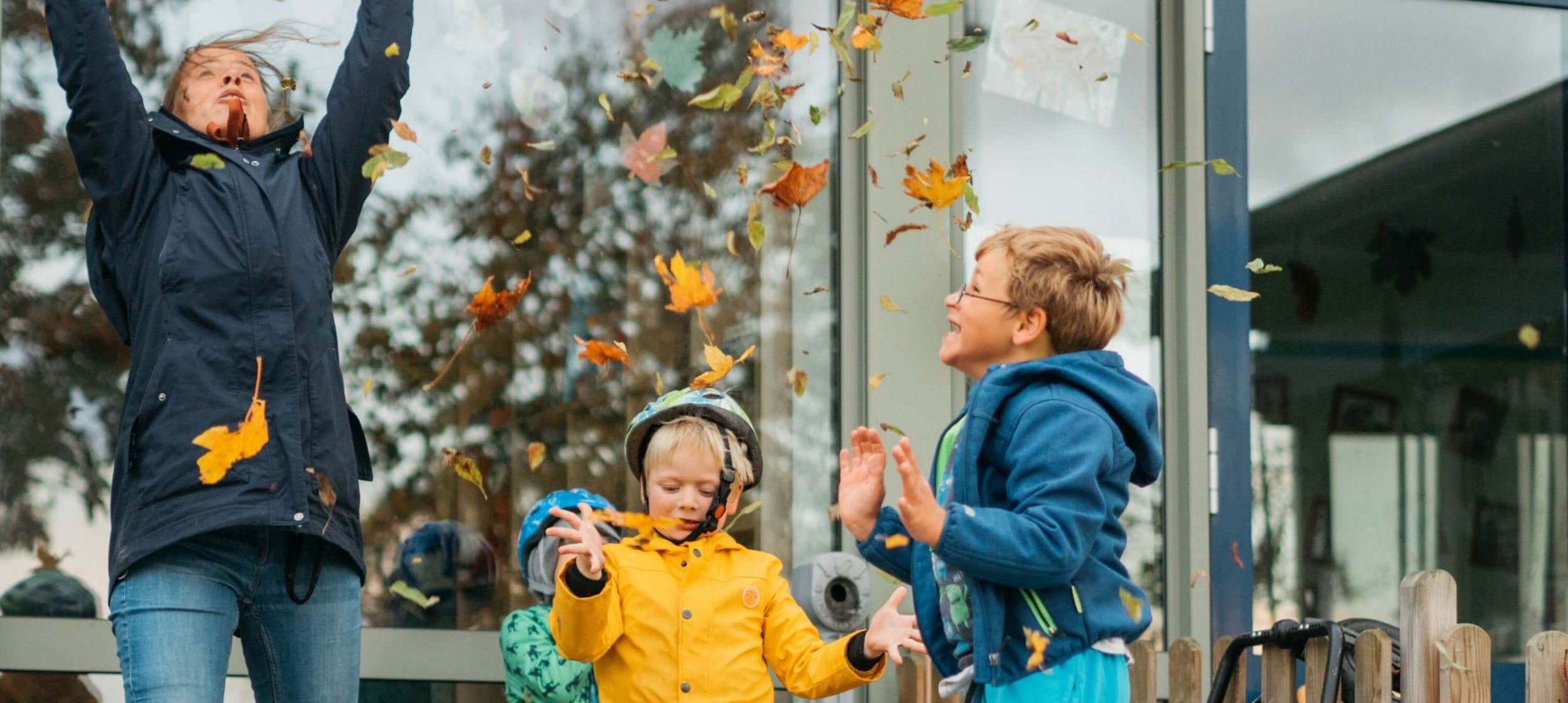 Eine erwachsene person und zwei Kinder werfen Herbst-Blätter in die Luft