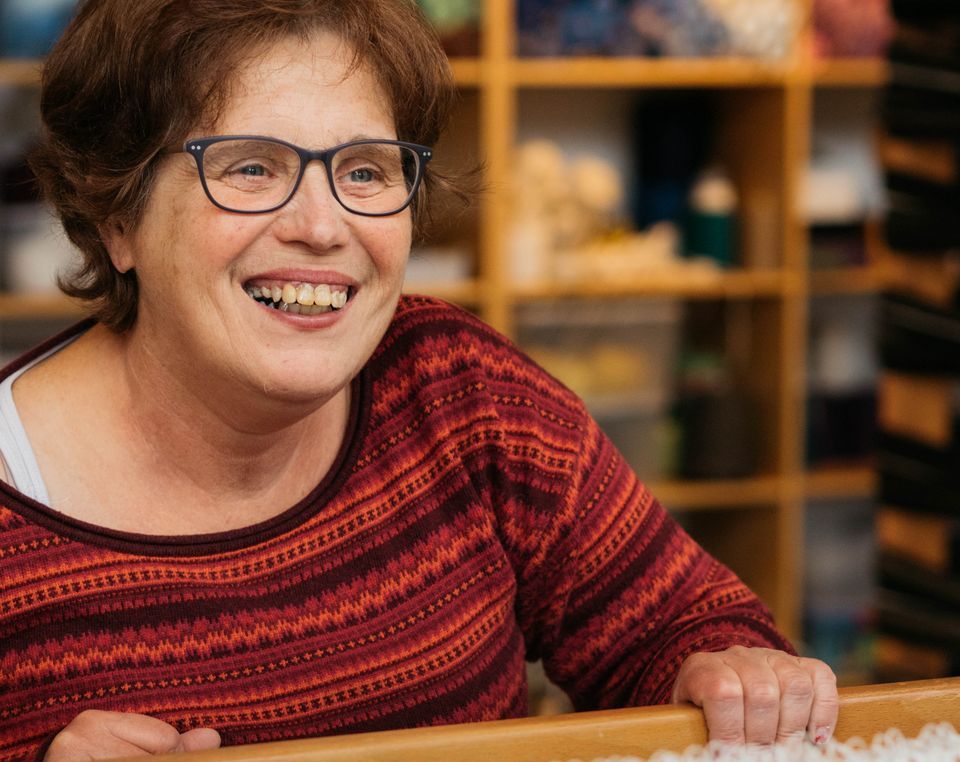 Brustbild einer lachenden Person mit Brille in der Weberei.