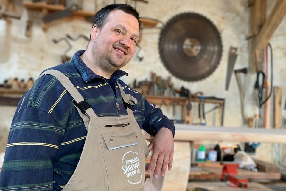 Mitarbeiter im historischen Sägewerk lacht in die Kamera