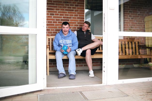 Eine Tür steht auf, zwei Menschen sitzen lachend auf einer Bank.
