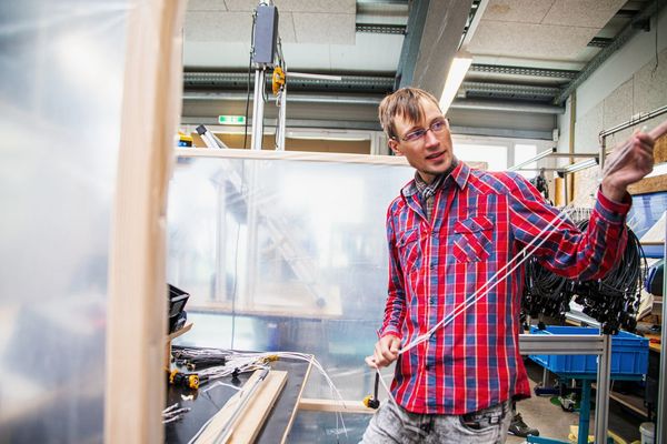 eine Person steht in einer Werkstatt und hält ein Kabel in der Hand