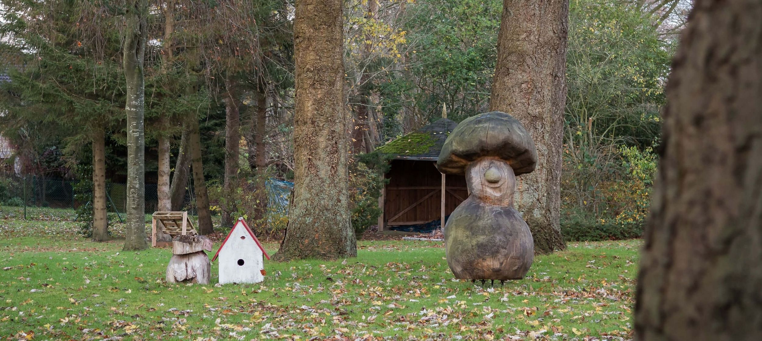 Im Garten unter Bäumen steht eine Holzskulptur eines Pilzes